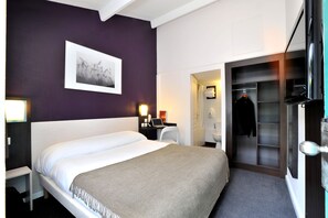 A hotel room with a bed, a desk with a laptop, a coat rack, and a walk-in closet. - Brit Hotel Confort Lyon Dardilly (Dardilly)