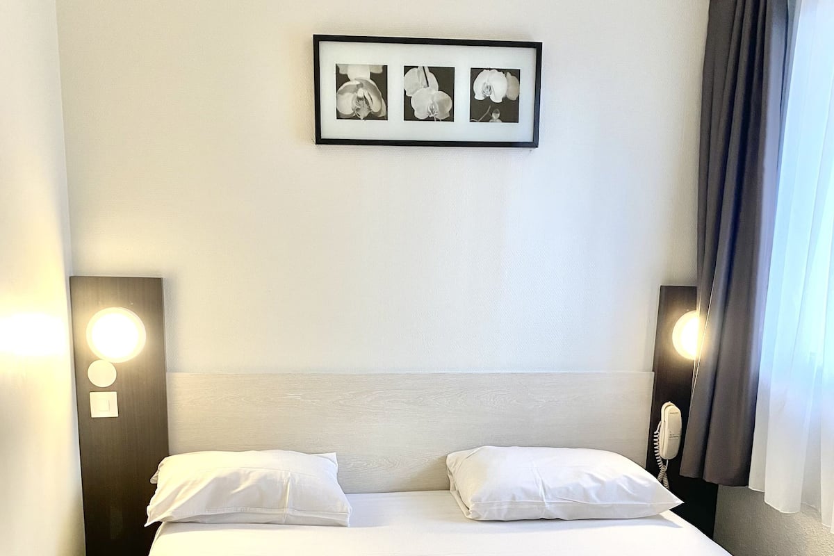 A hotel room with a neatly made bed, two bedside lamps, a framed picture on the wall, and a telephone on the nightstand.