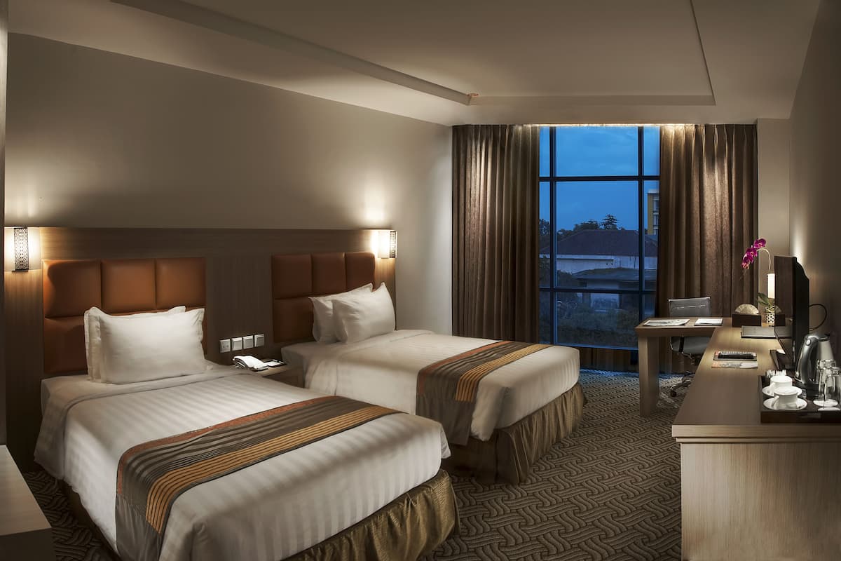 Une chambre d’hôtel avec deux lits, un bureau, une chaise et une grande fenêtre avec des rideaux.