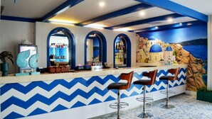 A bar area with a blue and white chevron pattern on the wall, three arched doorways, and a mural of a coastal scene.