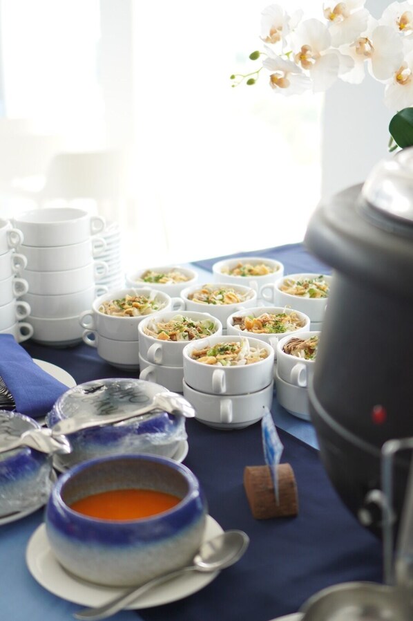 Una mesa con varias tazas blancas llenas de comida, un cuenco azul y blanco con sopa y una cafetera.