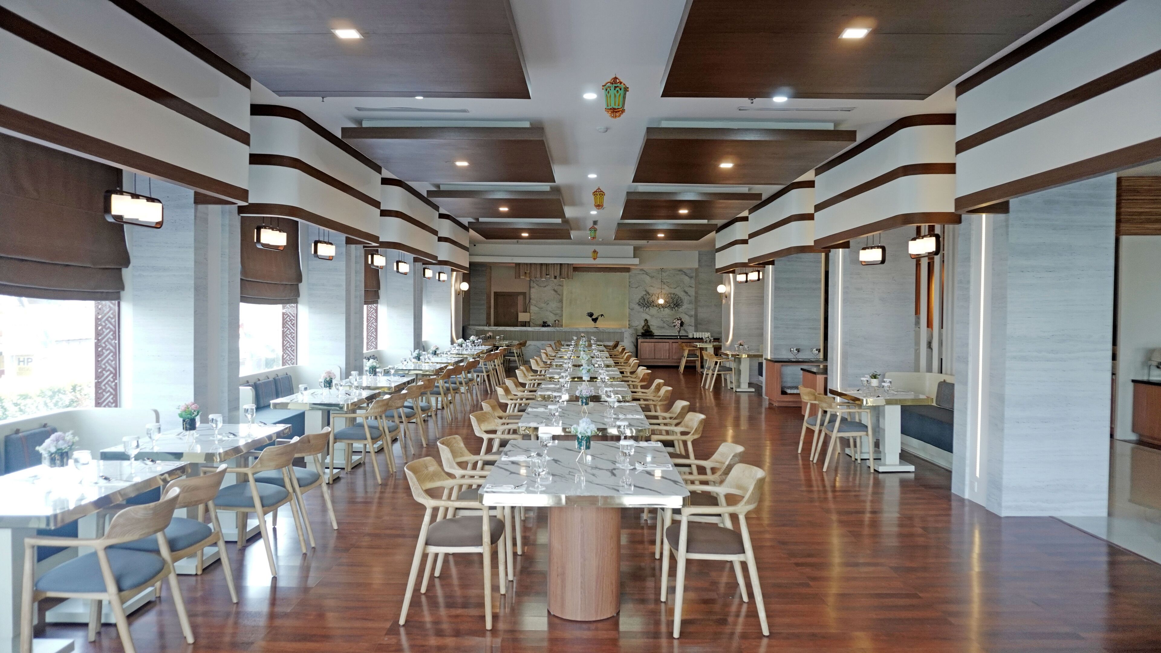 Un comedor amplio con mesas y sillas largas, un techo alto con iluminación empotrada y una pared decorativa con un mural de aves.