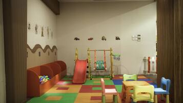 A children's playroom with a colorful play mat, a slide, a small swing set, and a ball pit.