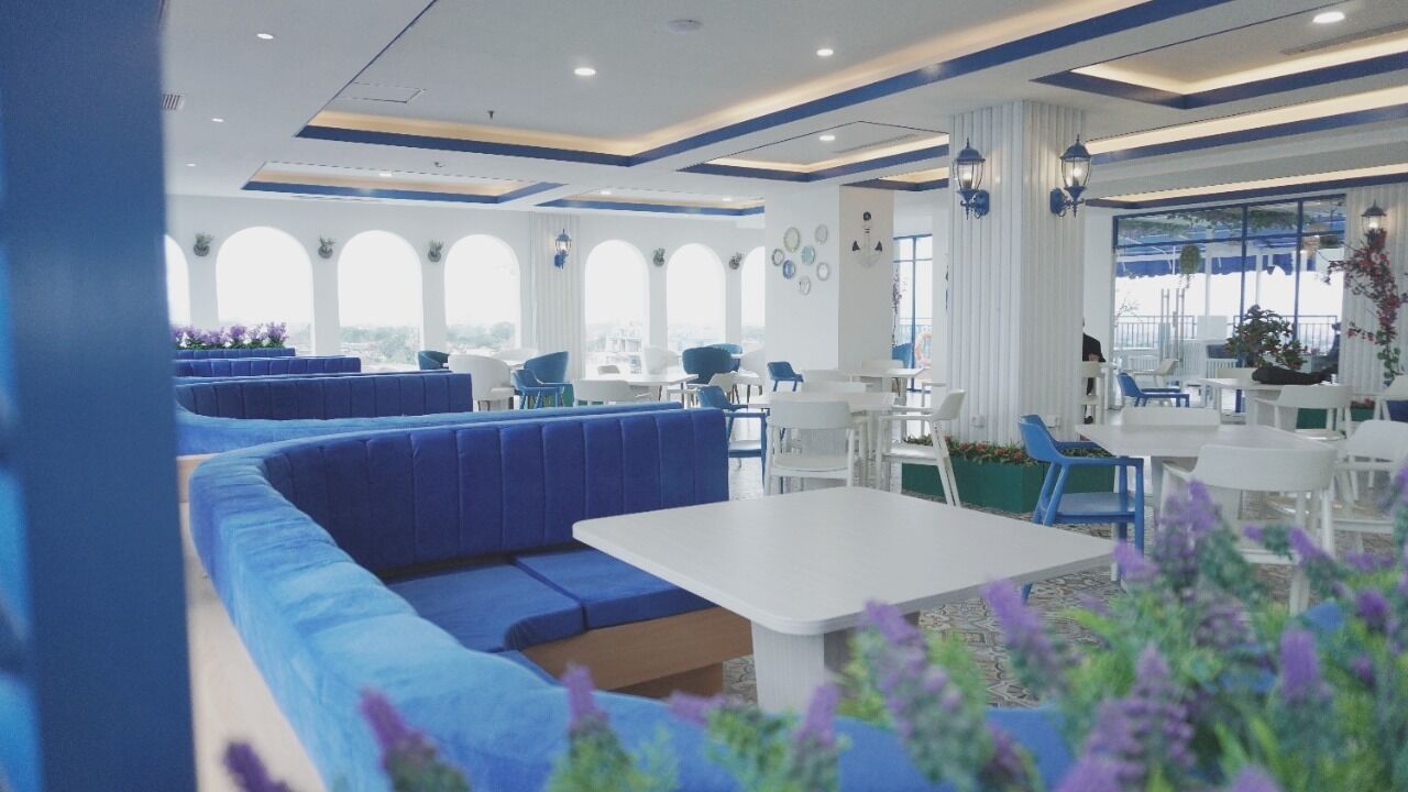 Un restaurant moderne avec des sièges bleus, des tables blanches et de grandes fenêtres.