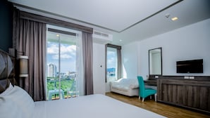 Habitación de hotel con una cama grande, un sofá, un televisor y un balcón con vista a la ciudad.
