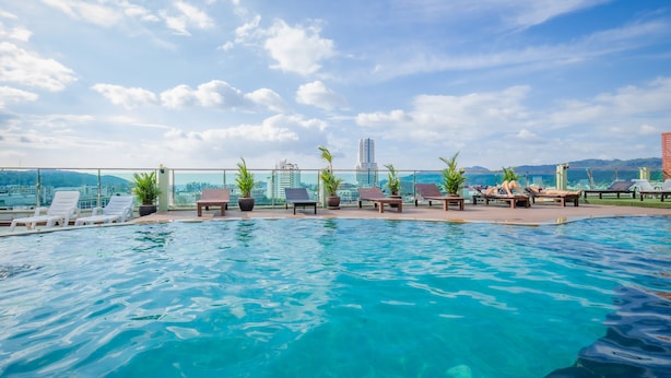 Una piscina en la azotea con sillones de descanso y plantas en macetas, con vistas a un paisaje urbano y montañas al fondo.