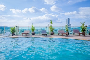 A rooftop infinity pool with lounge chairs and potted plants, overlooking a cityscape with tall buildings. - Add Plus Hotel & Spa (Patong)