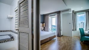 Habitación de hotel con una cama grande, una bañera, vista a la ciudad y un balcón.