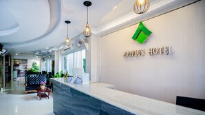 Un área de recepción moderna de hotel con un mostrador de mármol, un logotipo verde y una mesa de recepción.