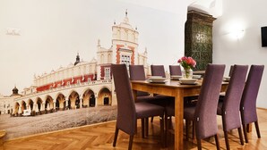 Uma sala de jantar com mesa de madeira e cadeiras roxas, um vaso de flores e um mural de um edifício histórico.