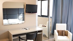Una habitación de hotel con cama, escritorio, silla, televisor y ventana con cortinas.