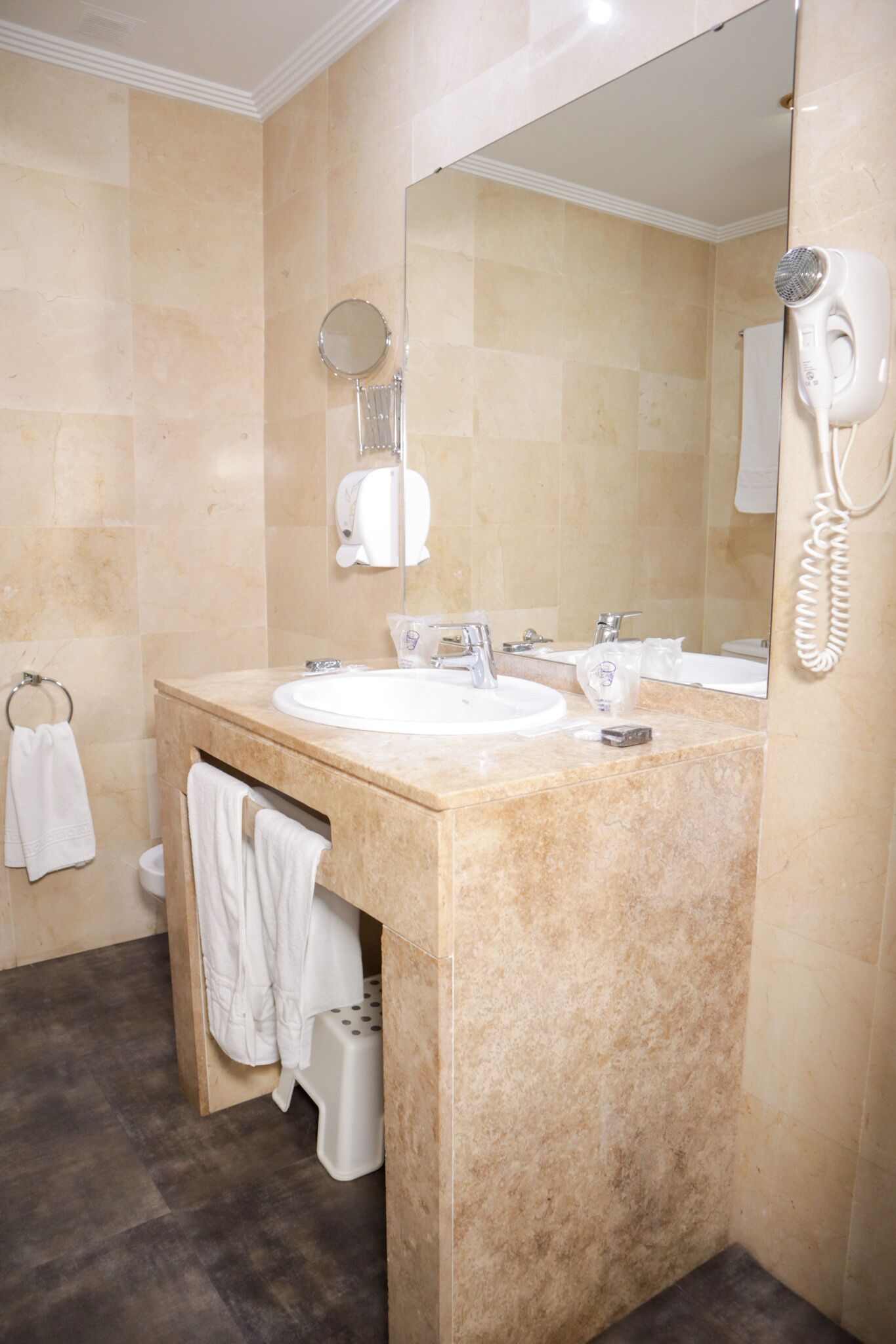 Un baño con lavamanos de mármol, un espejo, un secador de pelo y un perchero para toallas.