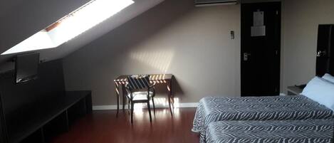 Una habitación con cama, un escritorio con silla, televisión y tragaluz.