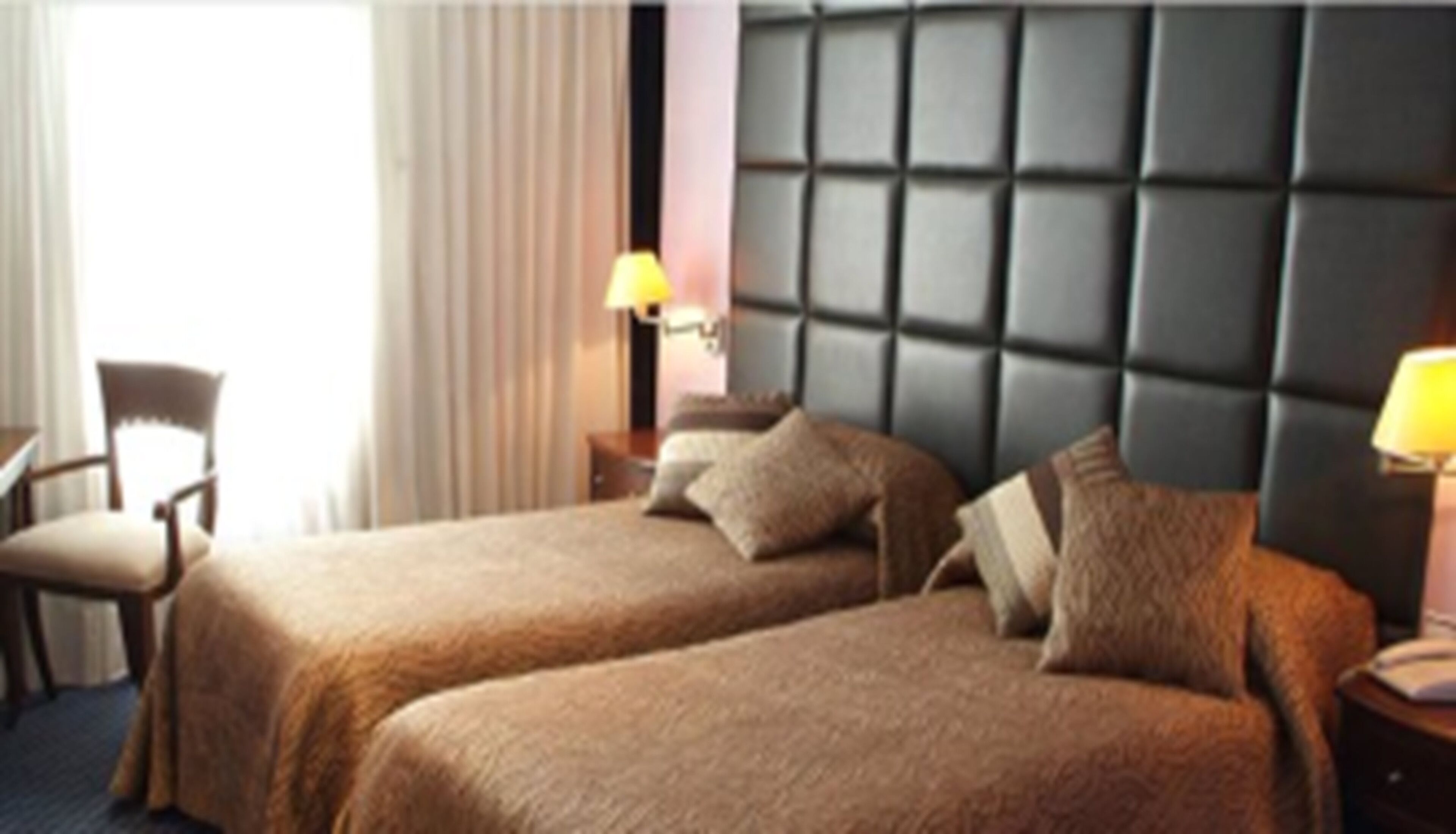 Une chambre d’hôtel avec deux lits, une chaise, une table de chevet et une fenêtre avec des rideaux.