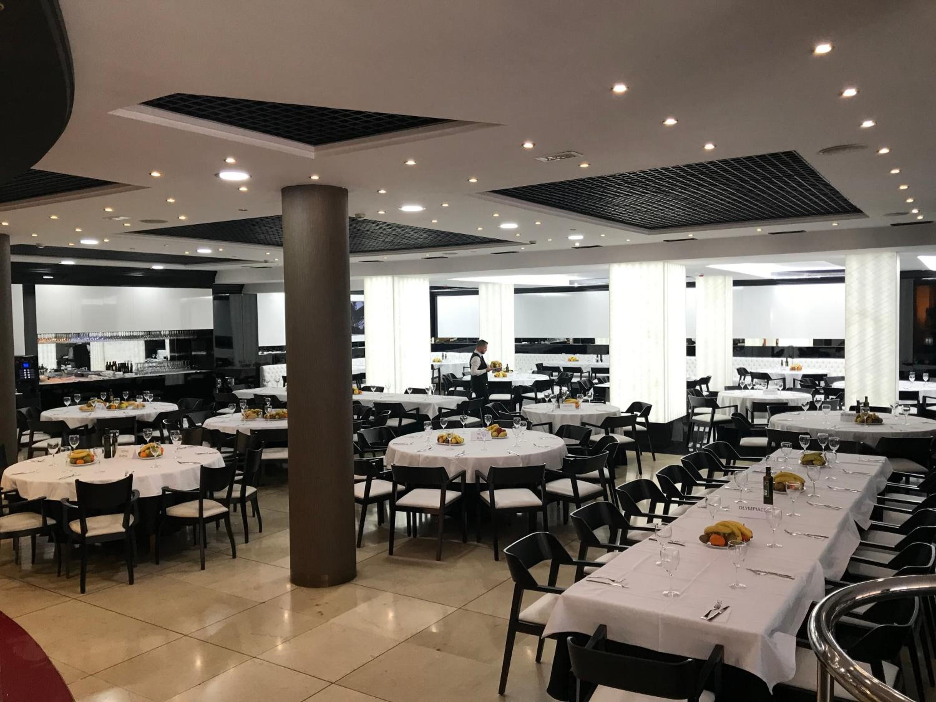 A spacious dining area with multiple round tables, each set with chairs and white tablecloths.