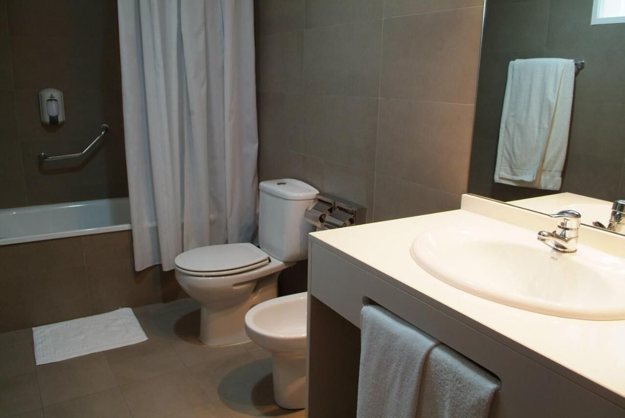 A bathroom with a bathtub, two toilets, a sink, and a mirror.