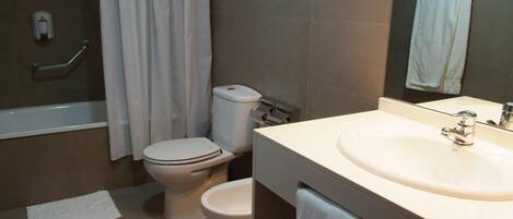 A bathroom with a bathtub, two toilets, a sink, and a mirror.