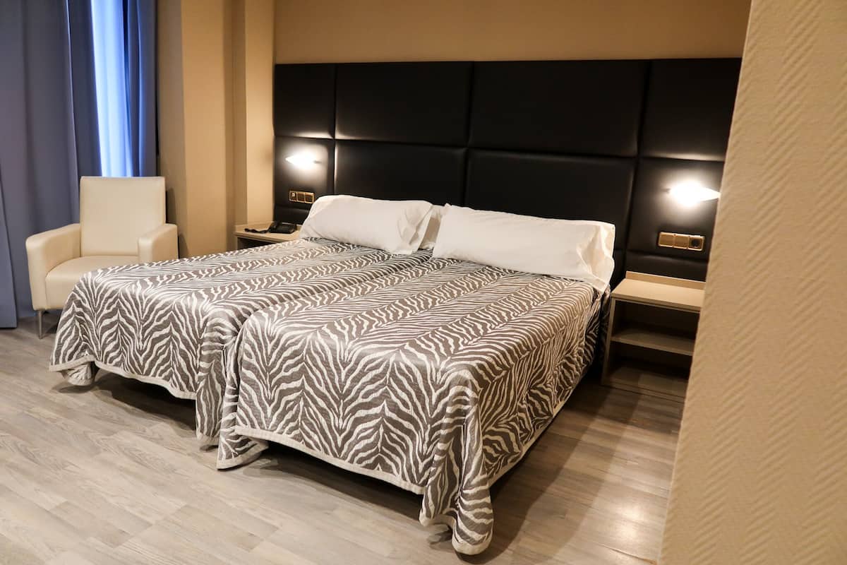 A hotel room with a large bed, a chair, bedside tables, and a modern headboard.