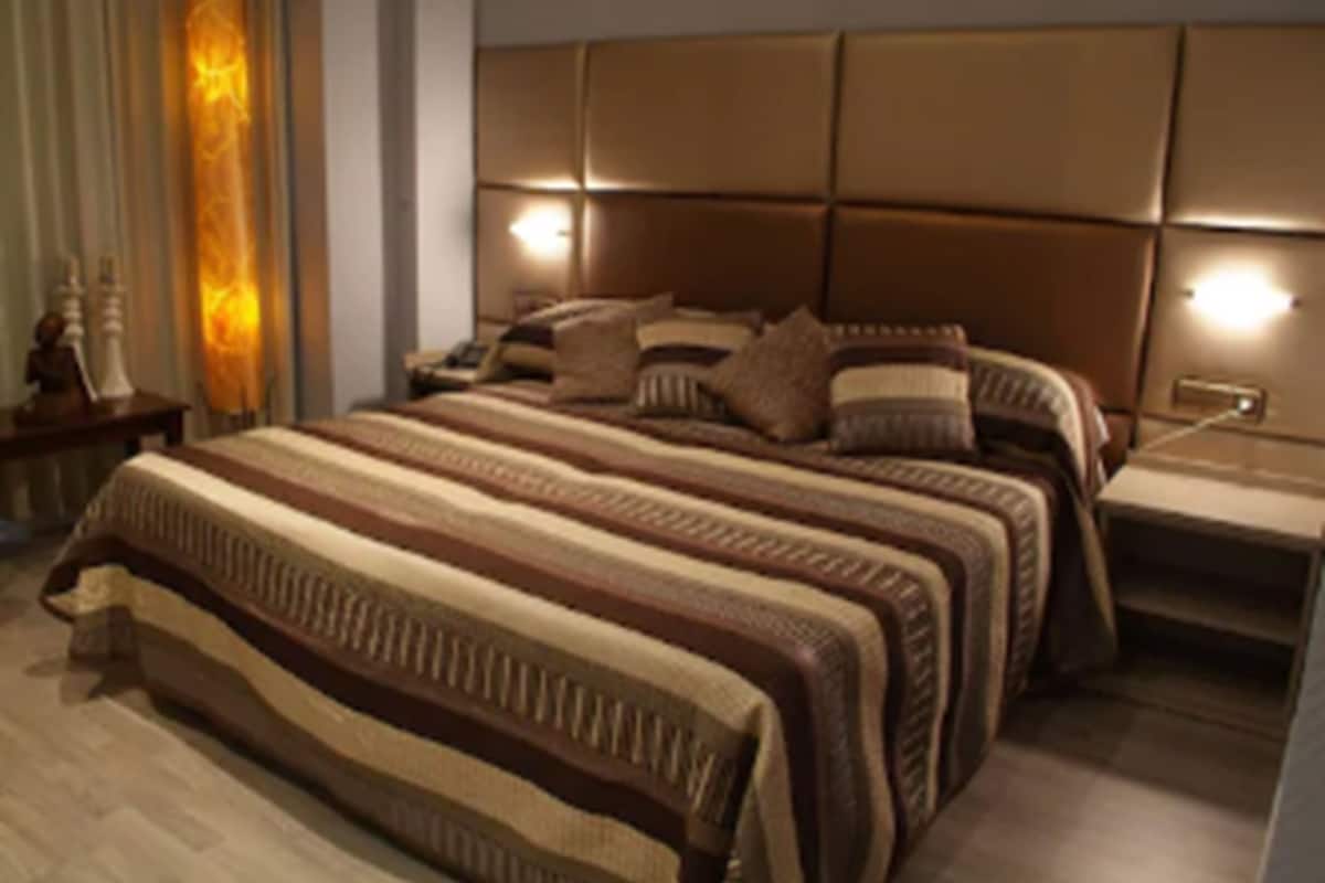 A modern bedroom with a large bed, a nightstand, and a wall-mounted lamp.