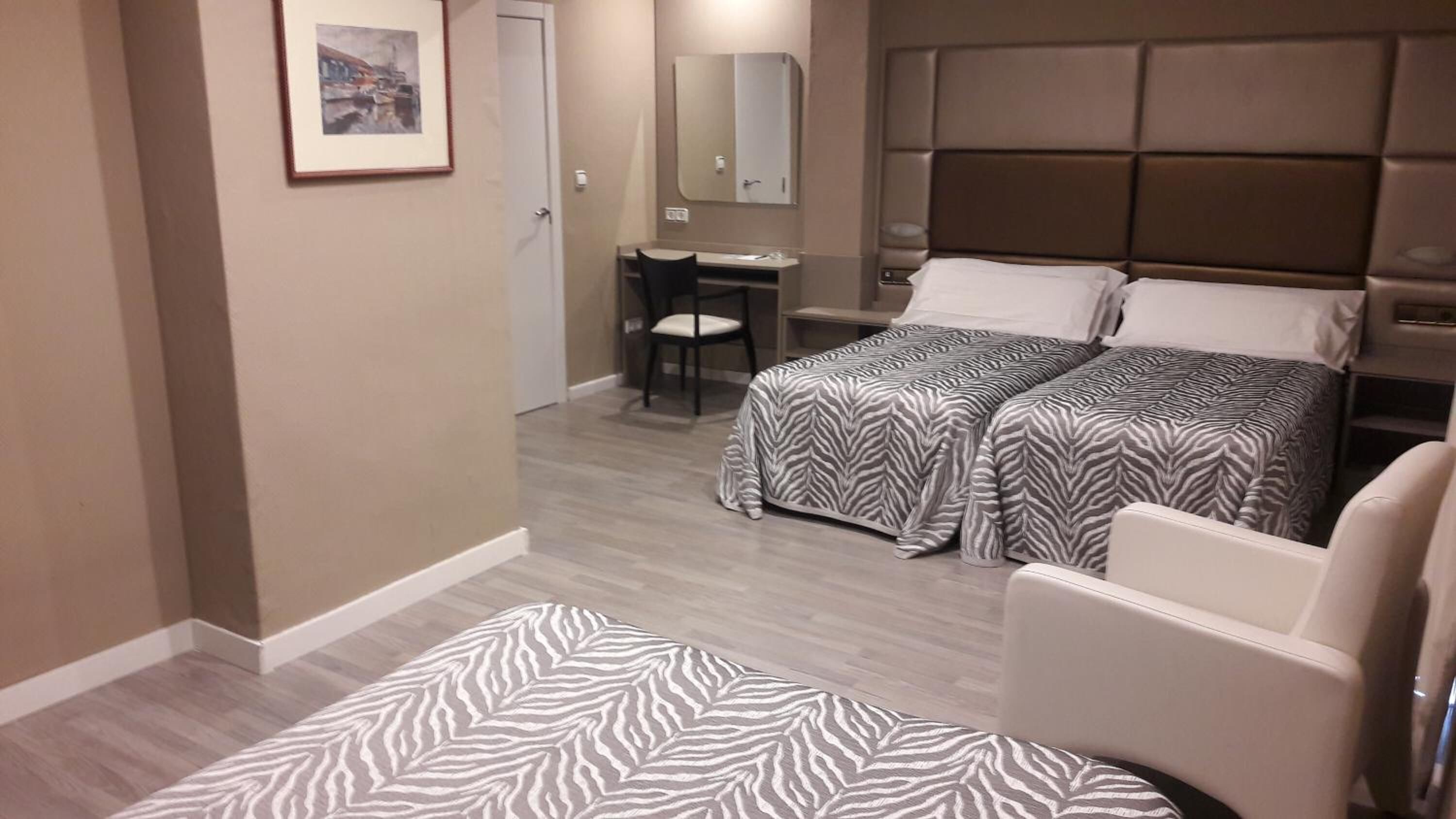 Habitación de hotel con dos camas, un escritorio, una silla y una alfombra con estampado de cebra.
