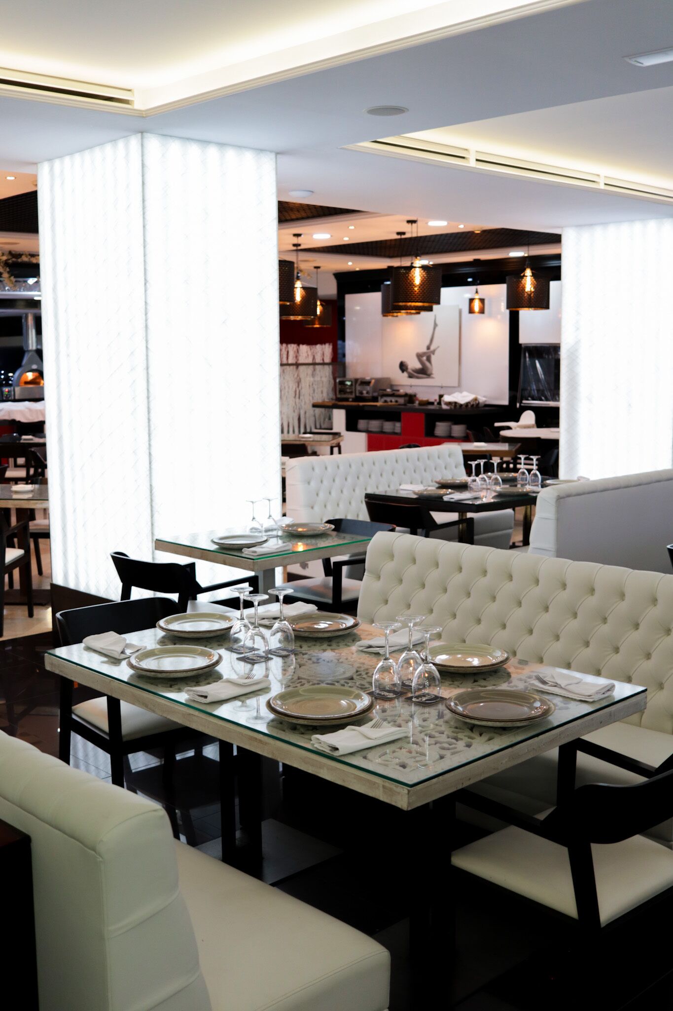 A dining area with a glass table set for four, surrounded by white upholstered chairs.