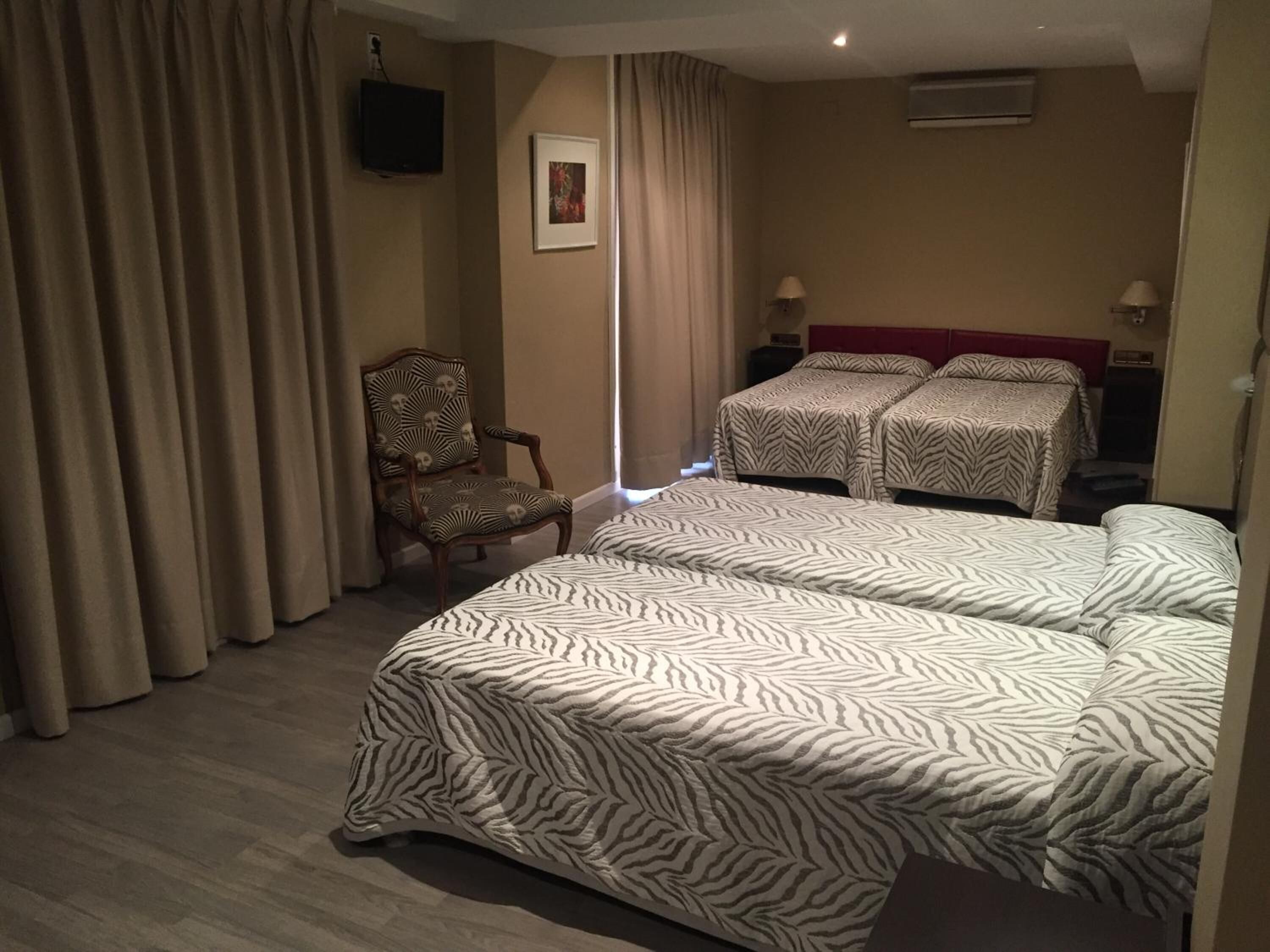 A hotel room with two beds, a chair, a television, and a window with curtains.