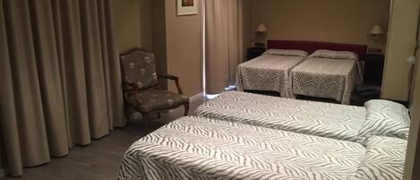 A hotel room with two beds, a chair, a television, and a window with curtains.