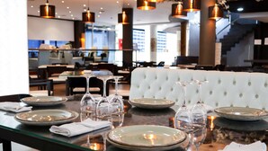 Comedor con mesa de vidrio dispuesta para seis personas, asientos acolchados blancos y lámparas colgantes.