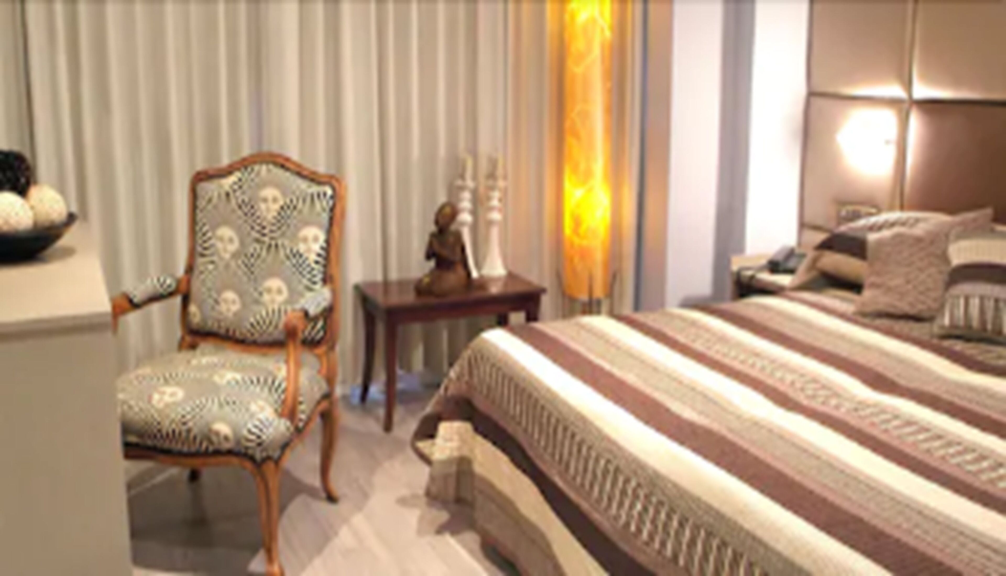 A hotel room with a large bed, a chair, a small table, and a lamp.