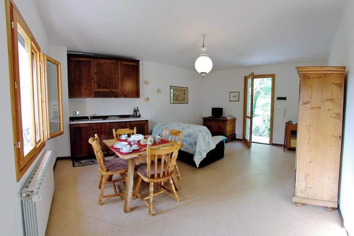 A compact room with a dining table, chairs, a bed, a wooden cabinet, and a radiator.