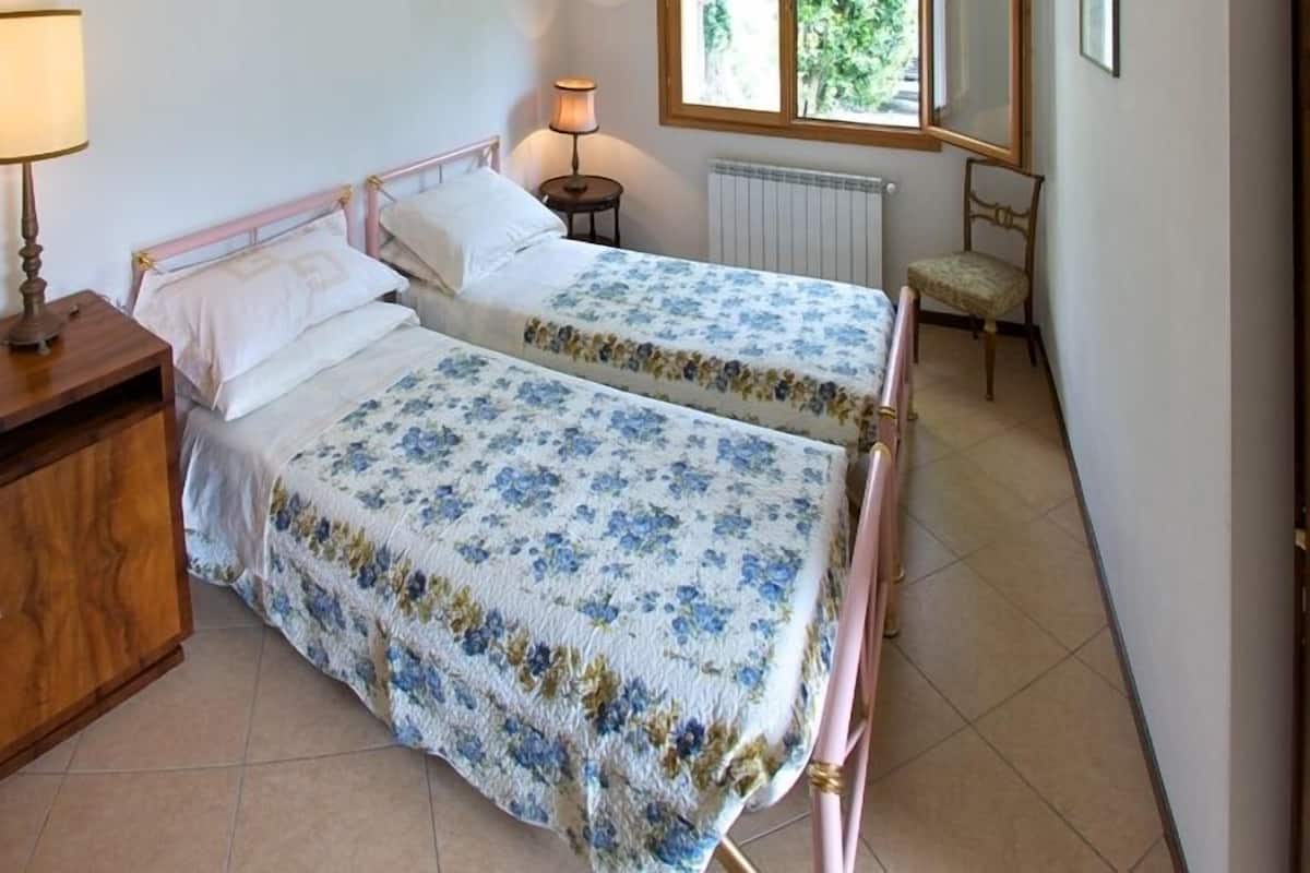 A bedroom with two single beds, a wooden dresser, a lamp, and a chair.