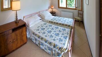Een slaapkamer met twee eenpersoonsbedden, een houten dressoir, een lamp en een stoel.