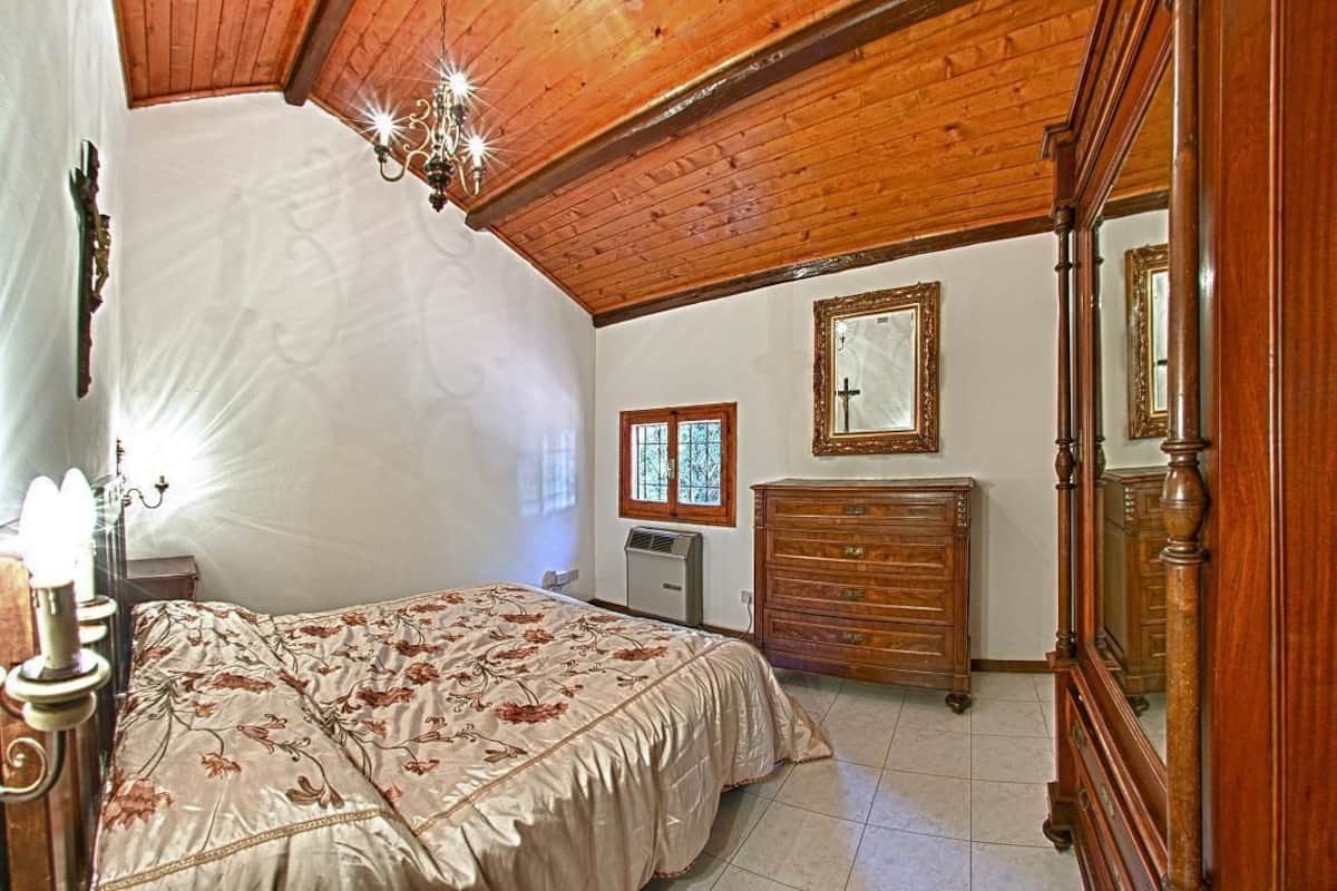A bedroom with a wooden ceiling, a bed with a floral bedspread, a dresser, and a mirror on the wall.