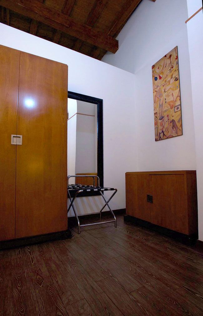 A room with wooden wardrobes, a metal chair, and a painting on the wall.