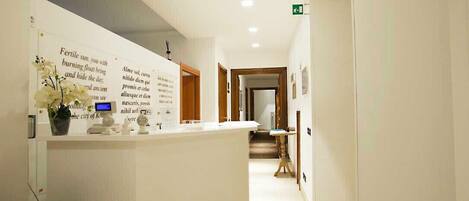 A reception area with a counter, a potted plant, and a digital display.