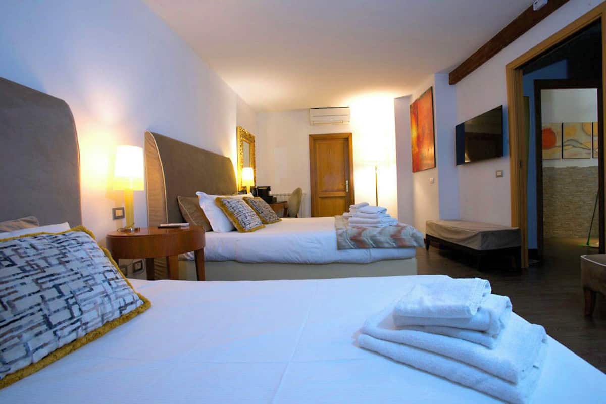 A hotel room with two beds, a sitting area, a TV, and artwork on the walls.