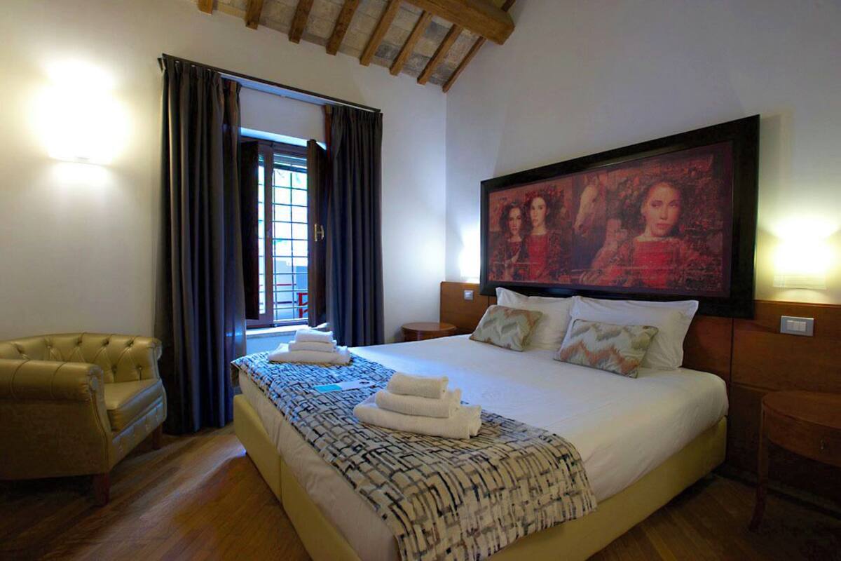 A hotel room with a large bed, a headboard with artwork, a sofa, and a window with curtains.