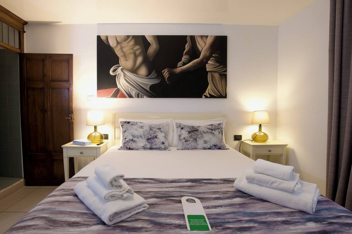 A hotel room with a bed, two nightstands, a painting above the bed, and towels on the bed.