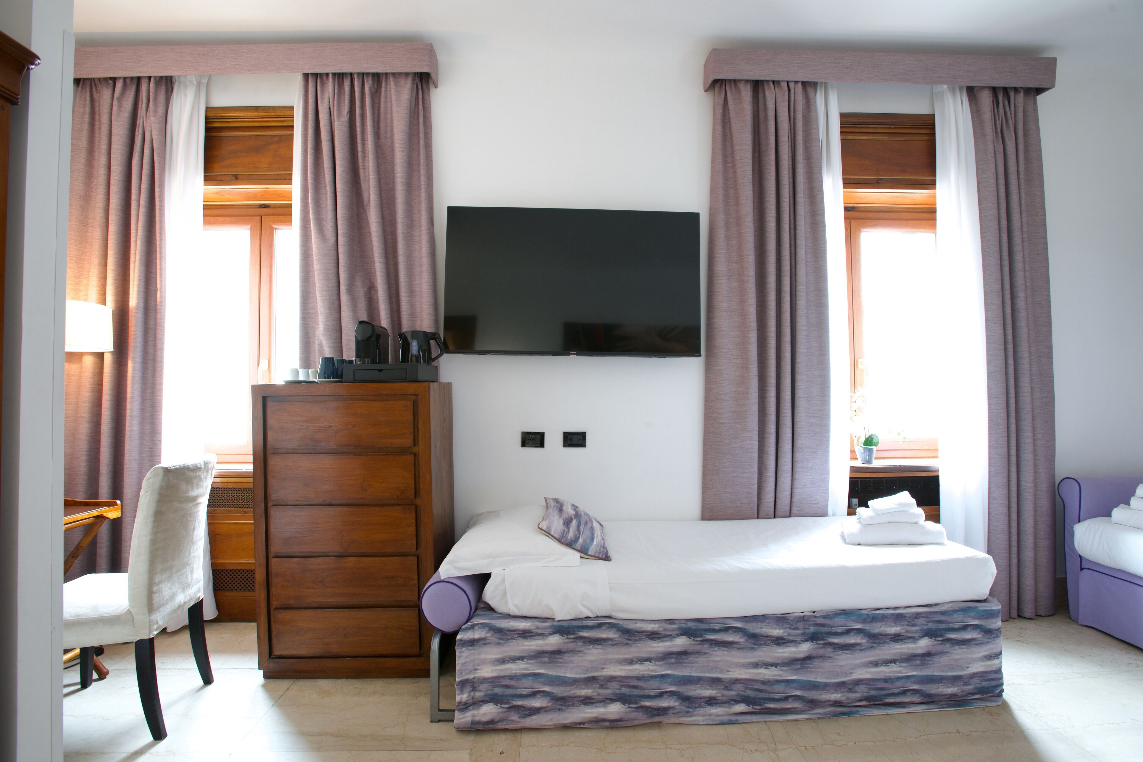 Un dormitorio con cama, televisor montado en la pared, escritorio y silla.