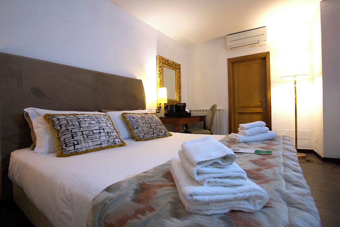 A hotel room with a bed, pillows, a desk, a chair, a lamp, and a door.