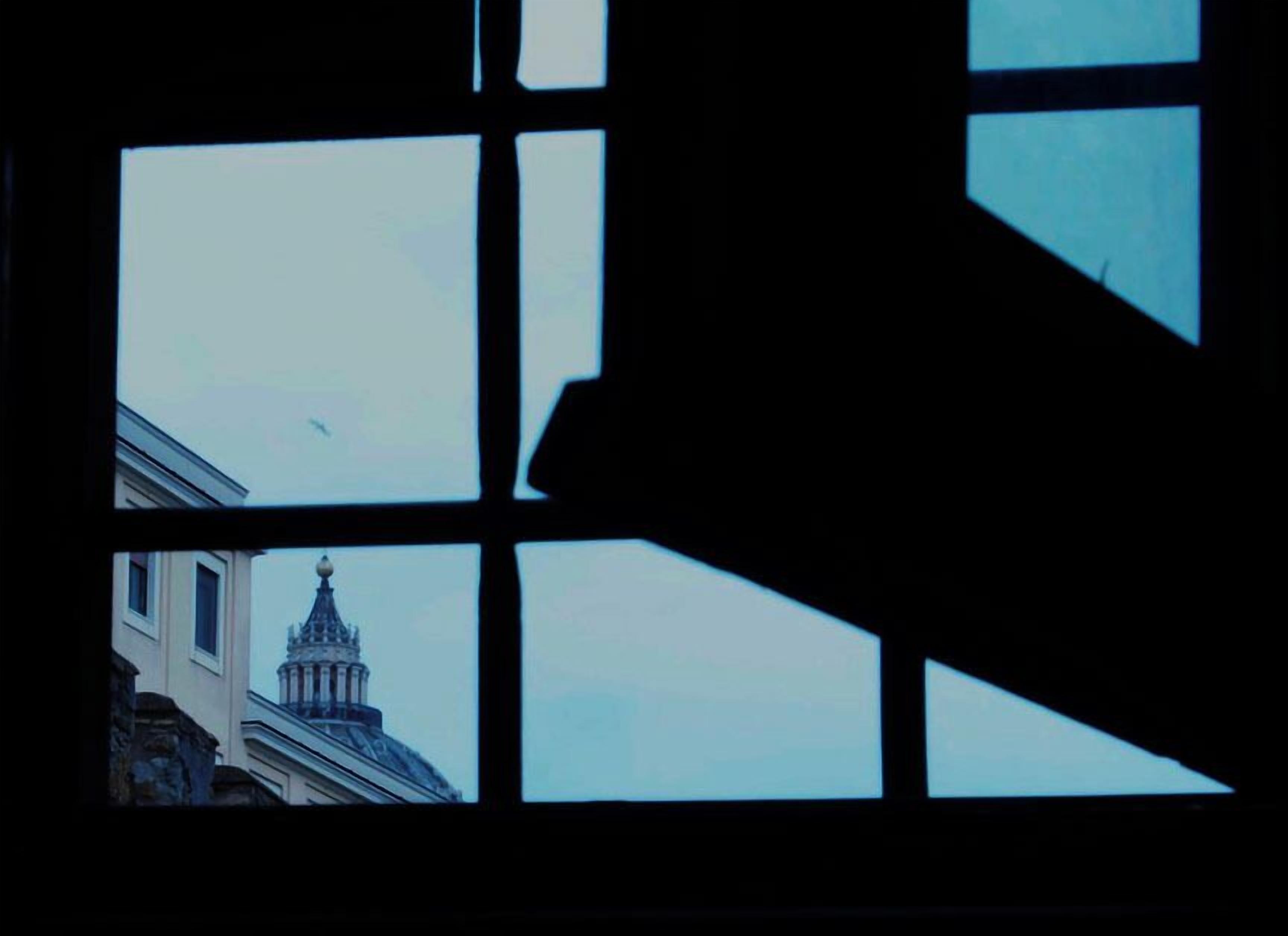 A view through a window with a geometric pattern, revealing a building with a dome and spire in the background.