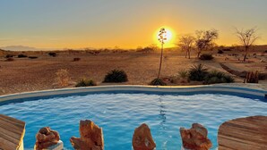 Ein Pool mit klarem, blauem Wasser, umgeben von Wüstenlandschaft und vereinzelter Vegetation.