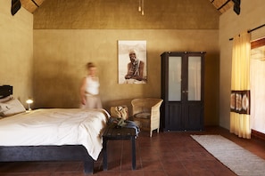 A bedroom with a bed, a wooden bench, a wicker chair, a wardrobe, and a poster on the wall.