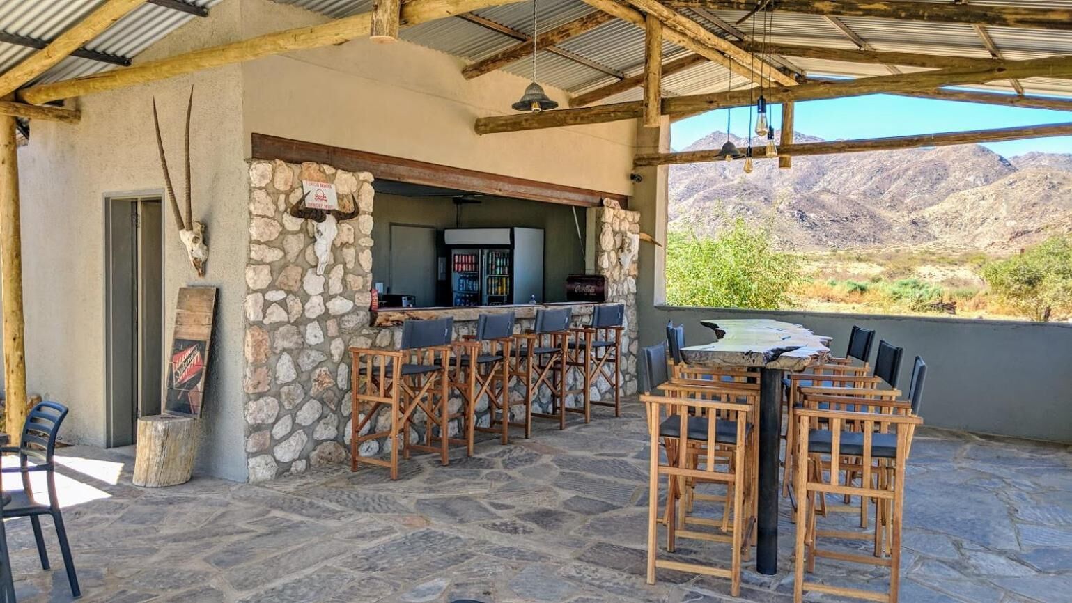 Patio esterno con pavimento in pietra, sedie in legno, angolo bar e parete in pietra.