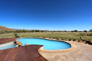 A swimming pool with a wooden deck, surrounded by a grassy landscape and distant mountains.