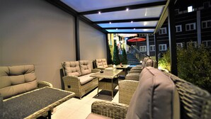 An outdoor patio with wicker furniture, including sofas and a table, under a glass roof. - Ascot Hotel (Remscheid)