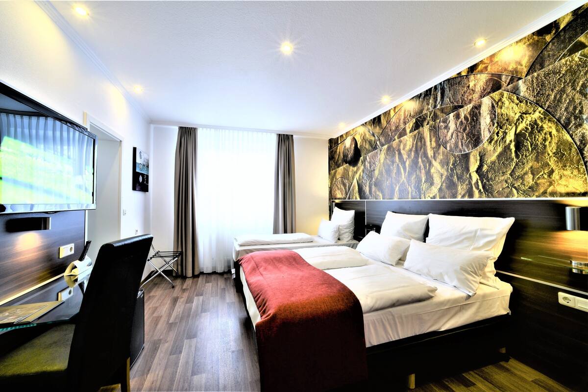 A hotel room with a bed, a desk, a chair, a TV, and a wall with a marble-like design.
