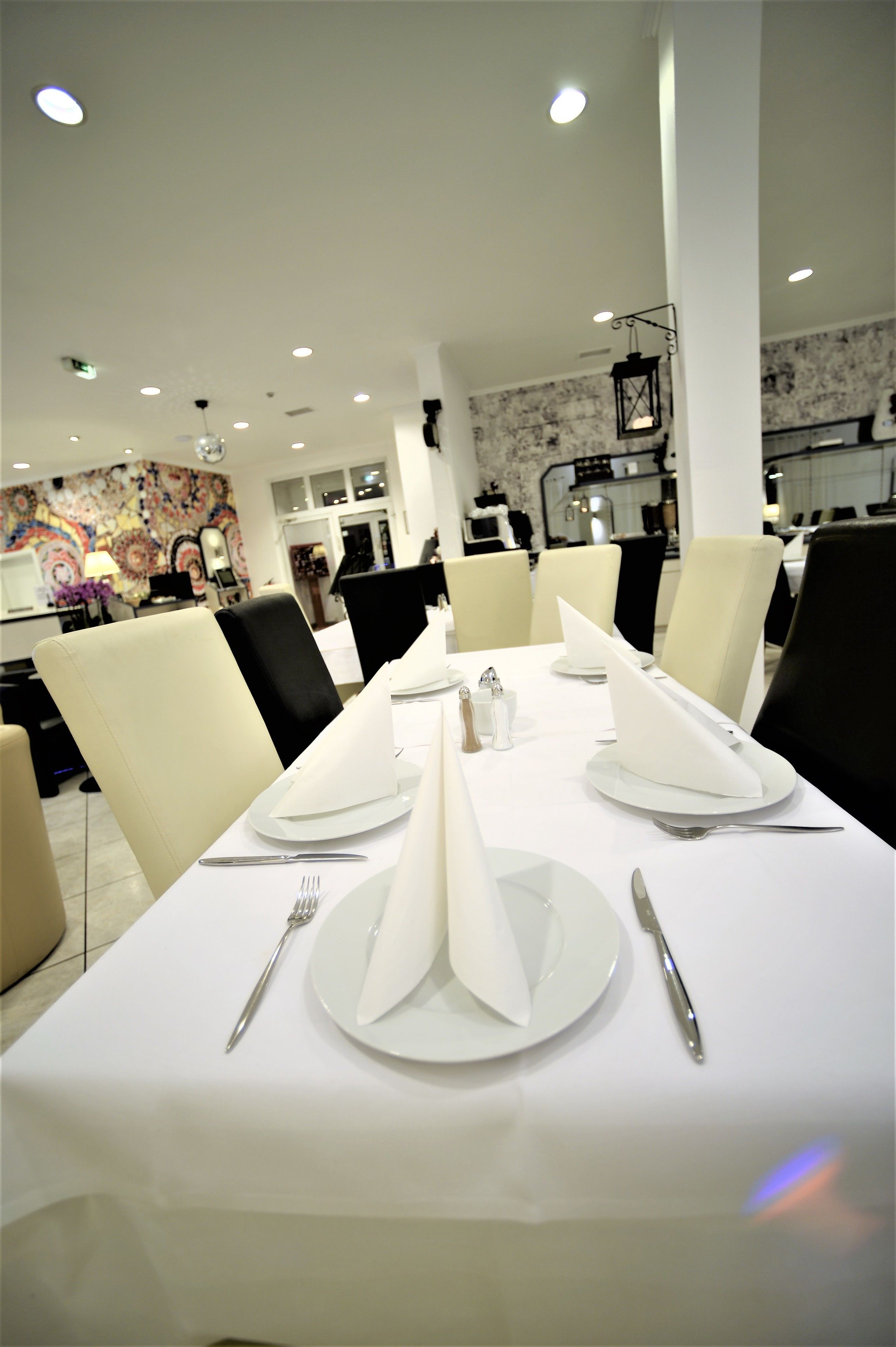 A dining area with white tablecloths, neatly set tables with plates, cutlery, and napkins.