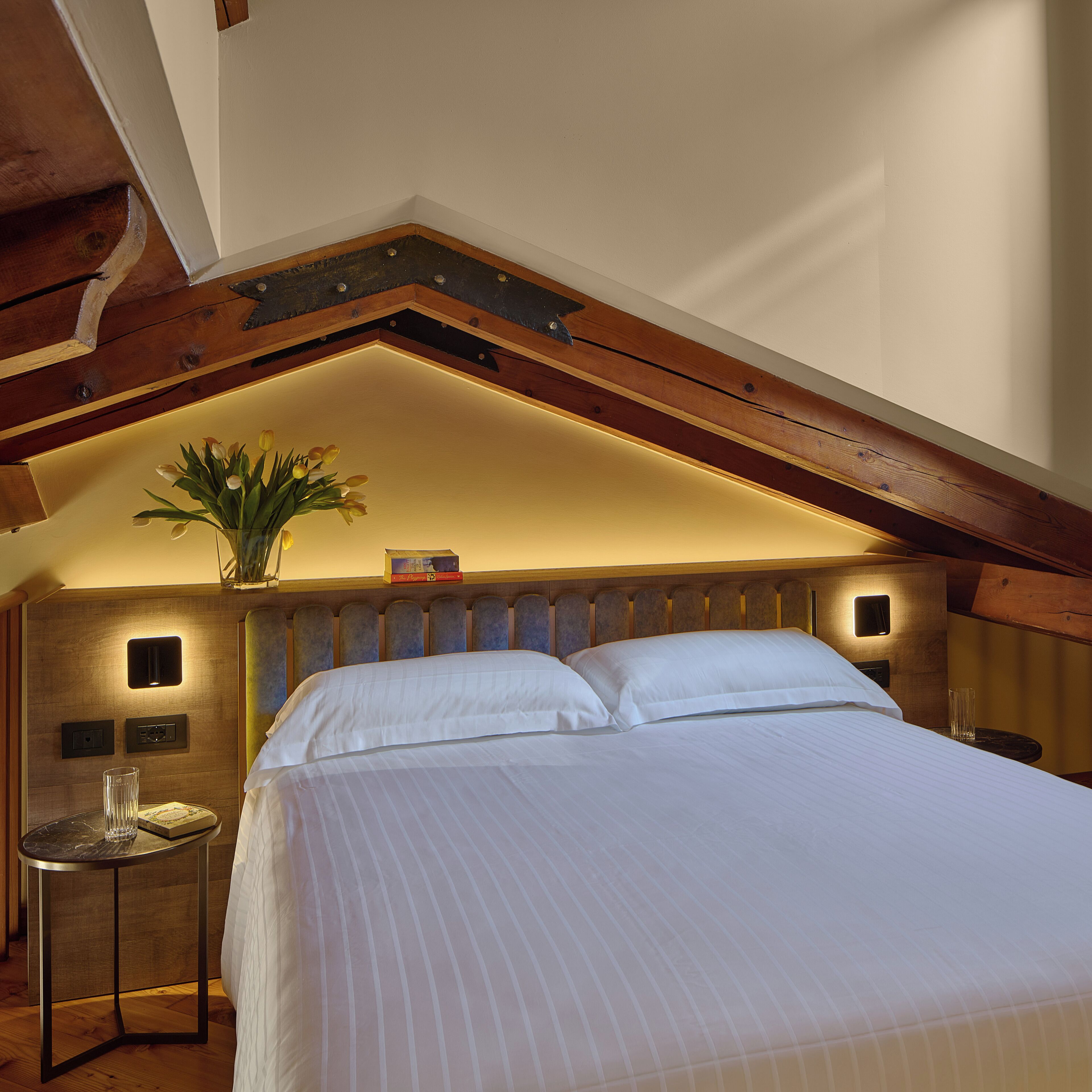 A bedroom with a large bed, a bedside table with a glass, and a small table with a book.