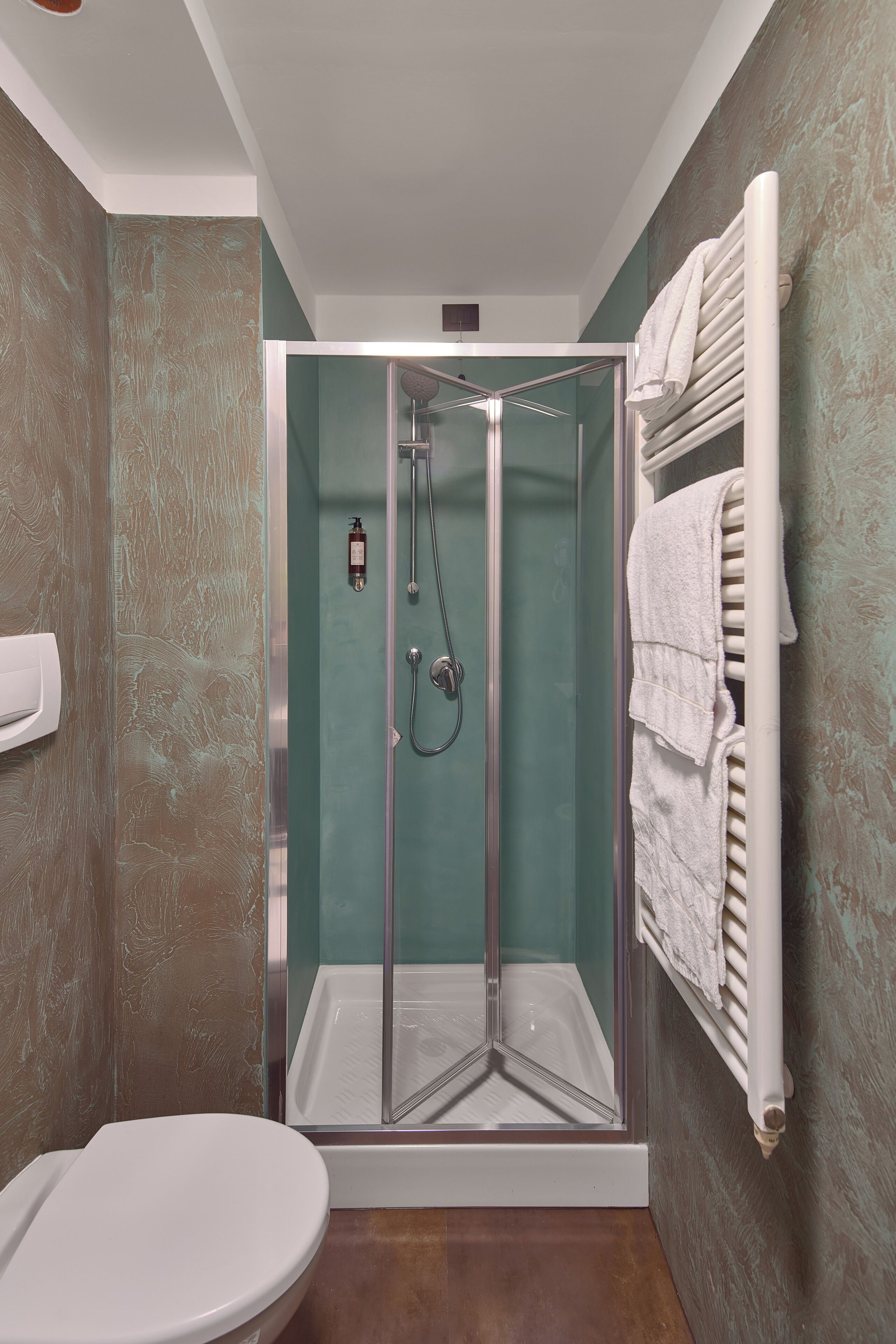A modern bathroom with a glass-enclosed shower, a white toilet, and a towel rack with folded towels.